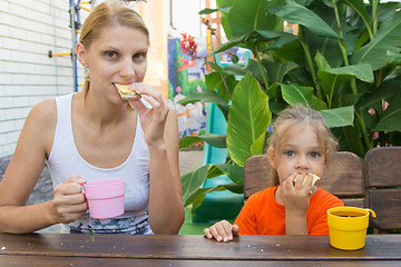 Image showing Mom and daughter having breakfast with tea and sandwiches sitting on the veranda