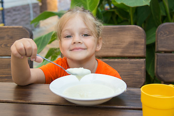Image showing Cheerful little girl eats porridge for breakfast