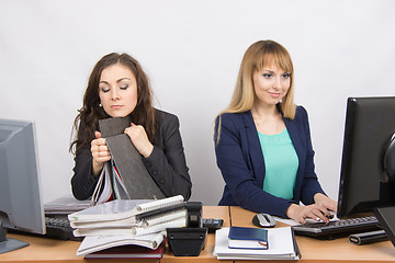 Image showing Female colleagues in the office, one asleep on a folder, the other happy working on a computer