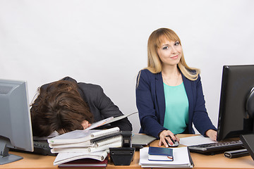 Image showing Female colleagues in the office, one had fallen asleep on a pile of folders, the other works in the computer and looked in the frame