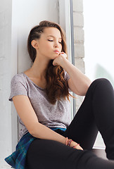 Image showing sad pretty teenage girl sitting on windowsill