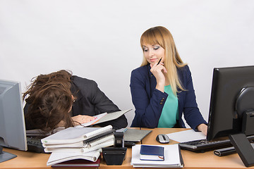 Image showing Female colleagues in the office, one had fallen asleep on a pile of folders, the second with a sneer looks at her