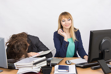 Image showing Female colleagues in the office, one had fallen asleep on a pile of folders, the other happily looking at the monitor screen