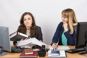 Image showing The situation in the office - one employee inundated with work and looking at the frame, the other does nothing, and with a smile looking at her