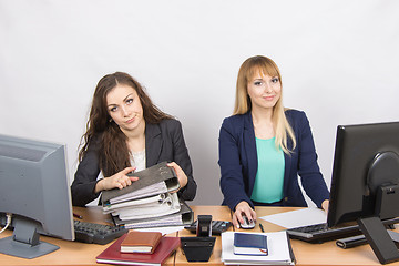 Image showing Female colleagues in the office, one littered with paper documents, the second sitting with a blank sheet of paper