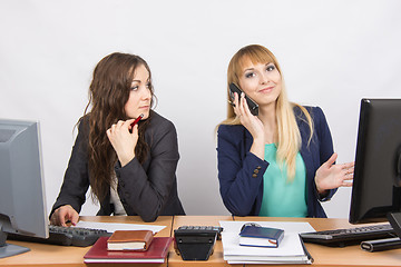 Image showing The situation in the office - a girl with a puzzled look on his colleague is talking on the phone