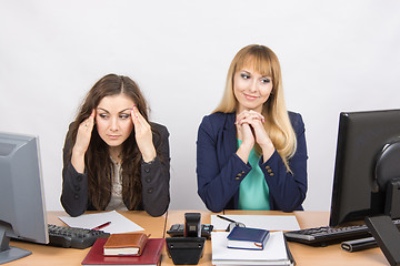 Image showing The situation in the office - girl happily looking at a computer screen, the other a girl with a headache looking at the screen