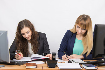 Image showing Two business women writing in paper documents sitting at a desk