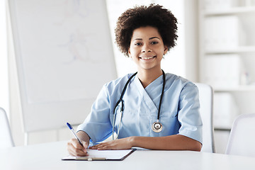 Image showing happy female doctor or nurse writing to clipboard