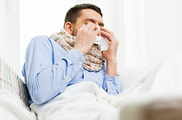Image showing ill man blowing nose with paper napkin at home