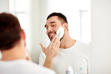 Image showing happy man applying shaving foam at bathroom mirror