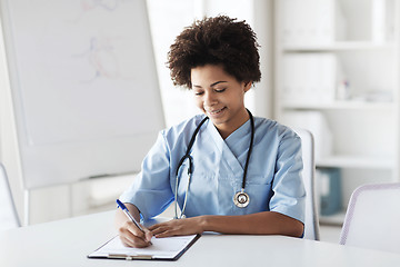 Image showing happy female doctor or nurse writing to clipboard