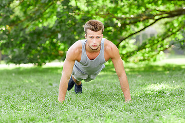 Image showing young man doing push ups on grass in summer park