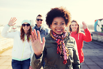 Image showing happy teenage friends waving hands on city street