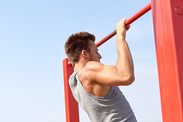 Image showing young man exercising on horizontal bar outdoors