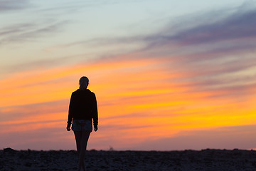 Image showing Woman on rocky beach watching sunset.