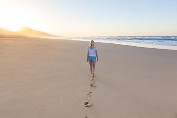 Image showing Lady walking on sandy beach in sunset.