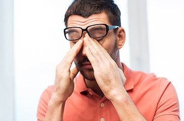 Image showing tired man in eyeglasses rubbing eyes at home