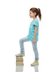 Image showing happy little girl stepping on book pile