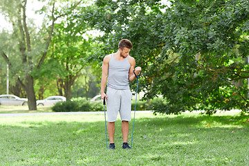 Image showing young man exercising with expander in summer park