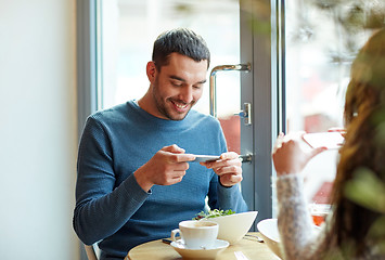 Image showing happy couple picturing food by smartphone at cafe