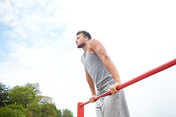 Image showing young man exercising on horizontal bar outdoors