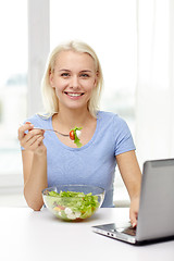 Image showing smiling woman with laptop eating salad at home