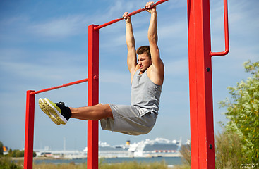 Image showing young man exercising on horizontal bar outdoors