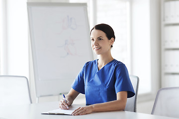 Image showing happy female doctor or nurse writing to clipboard