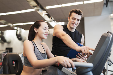 Image showing happy woman with trainer on exercise bike in gym