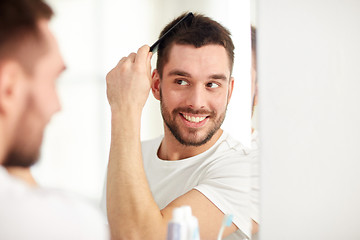 Image showing happy man brushing hair  with comb at bathroom