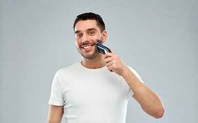 Image showing smiling man shaving beard with trimmer over gray