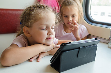 Image showing Two girls on a train with interest looking cartoon Tablet PC