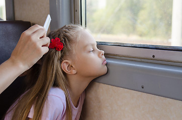 Image showing A sad little girl looks at the window while sitting in an electric train until my mother combs her long hair