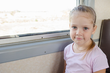 Image showing Happy girl sitting on a chair by the window in a suburban electric train