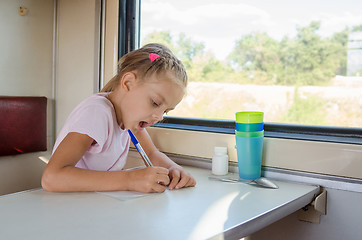 Image showing Girl draws a pen on a sheet of paper in a second-class train carriage