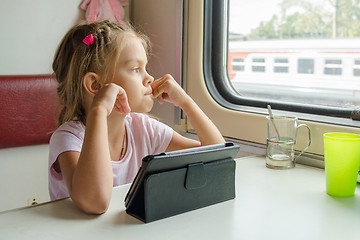 Image showing Girl thoughtfully looked out the window while sitting with a tablet on a train