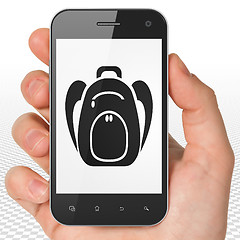 Image showing Vacation concept: Hand Holding Smartphone with Backpack on display