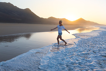 Image showing Lady enjoying running from waves on sandy beach in sunset.