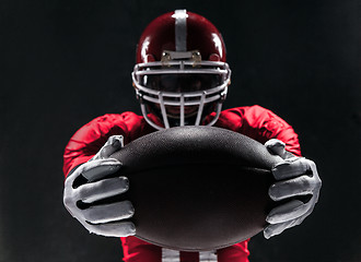 Image showing American football player posing with ball on black background