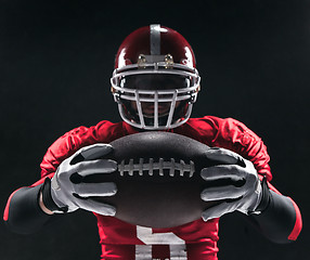 Image showing American football player posing with ball on black background