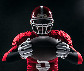 Image showing American football player posing with ball on black background