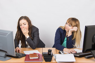 Image showing Two young office employee wearily sitting behind a desk