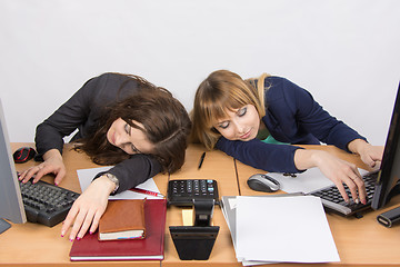 Image showing Two young office employee asleep on desk for computers