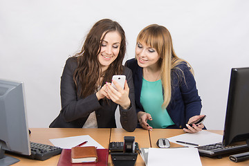 Image showing Two branchless workers enthusiastically looking at cell phone at his desk