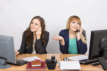 Image showing Two girls at a desk talking on mobile phone in the office