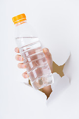 Image showing Woman hand with bottle of water through a hole in paper