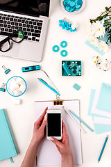 Image showing The female hands and smart phone against blue objects on white