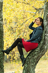 Image showing Pretty woman sits on tree in autumn park