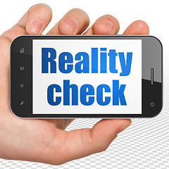 Image showing Finance concept: Hand Holding Smartphone with Reality Check on display